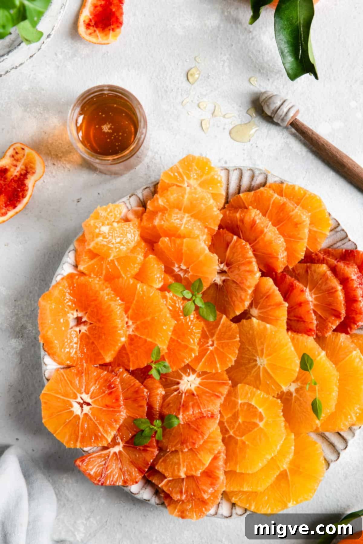A close-up of a plate filled with beautifully sliced assorted citrus fruits, with a small jar of honey beside it