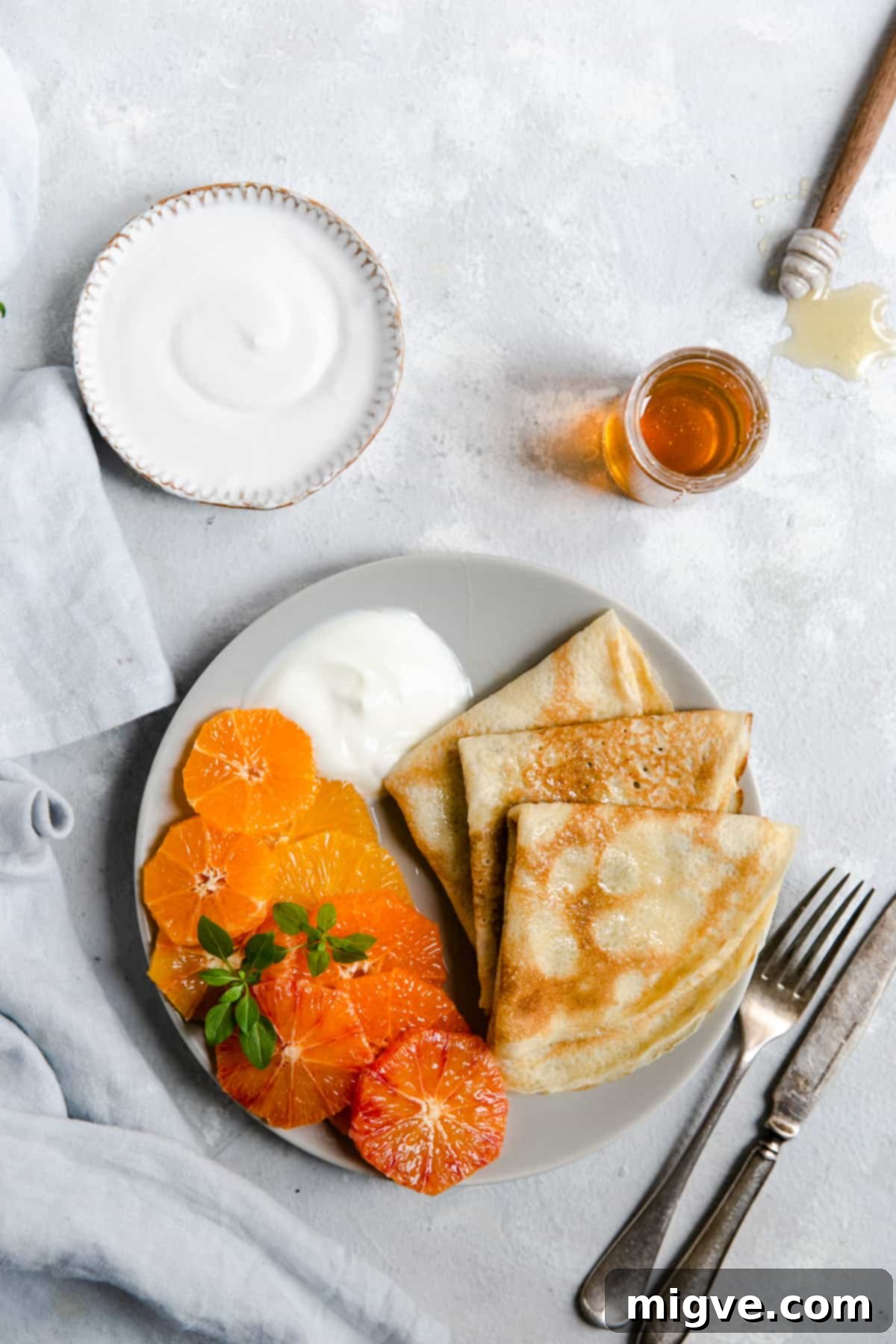 A beautifully presented plate featuring three crepes folded into triangles, adorned with fresh citrus slices and a spoonful of creamy yogurt