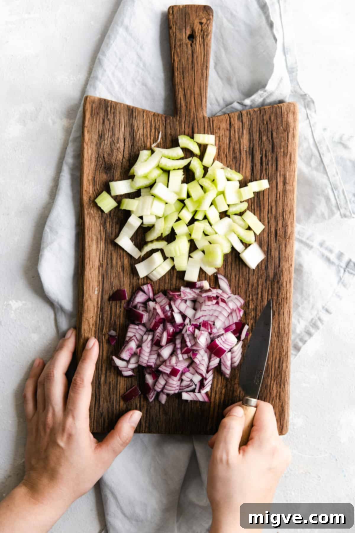 Overhead view of freshly chopped celery and onion on a rustic wooden chopping board, ready for the soup