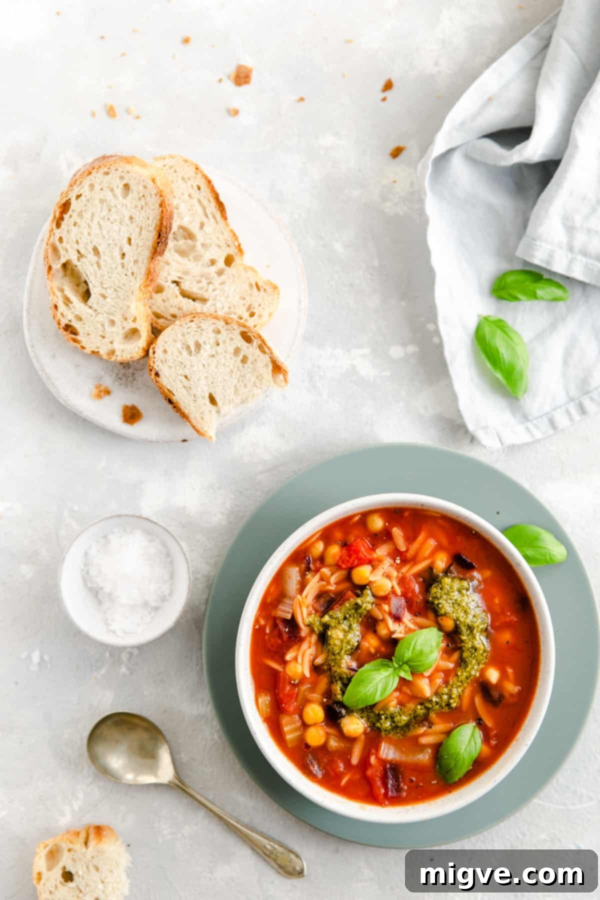 Overhead shot of a inviting bowl of Orzo and Tomato Soup, with slices of crusty bread on the side for dipping