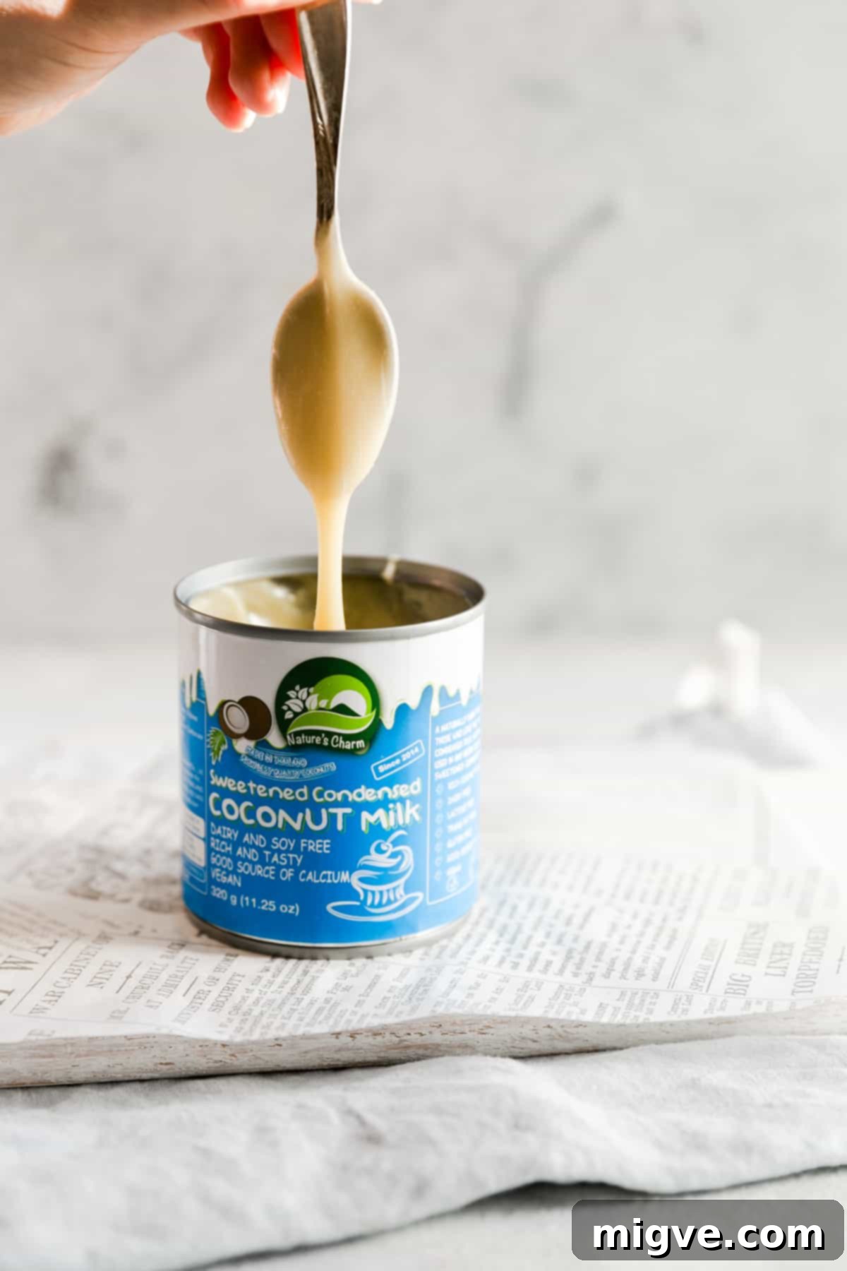 straight ahead shot of spoon covered in condensed coconut milk dripping into the can