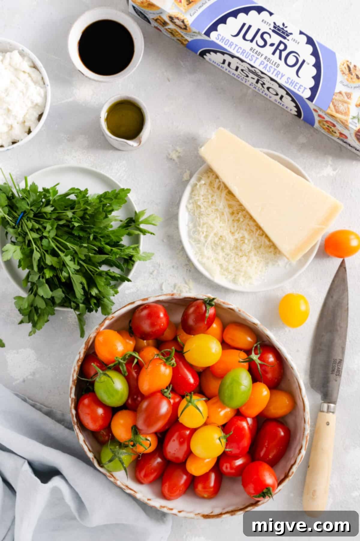 Vibrant Tomato & Savory Cheese Tartlets 4 An overhead shot showcasing all the fresh ingredients needed for mixed tomato and cheese tartlets: puff pastry, colorful mixed baby plum tomatoes, creamy ricotta, vegetarian hard cheese, fresh parsley, extra virgin olive oil, and balsamic glaze.
