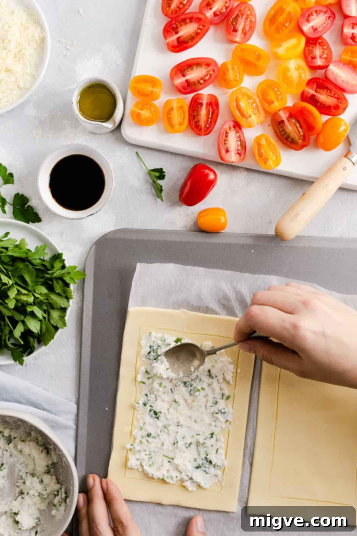 Vibrant Tomato & Savory Cheese Tartlets 5 Overhead shot of a person gently spreading the soft ricotta and hard cheese mixture over the unbaked puff pastry, staying within the scored border.