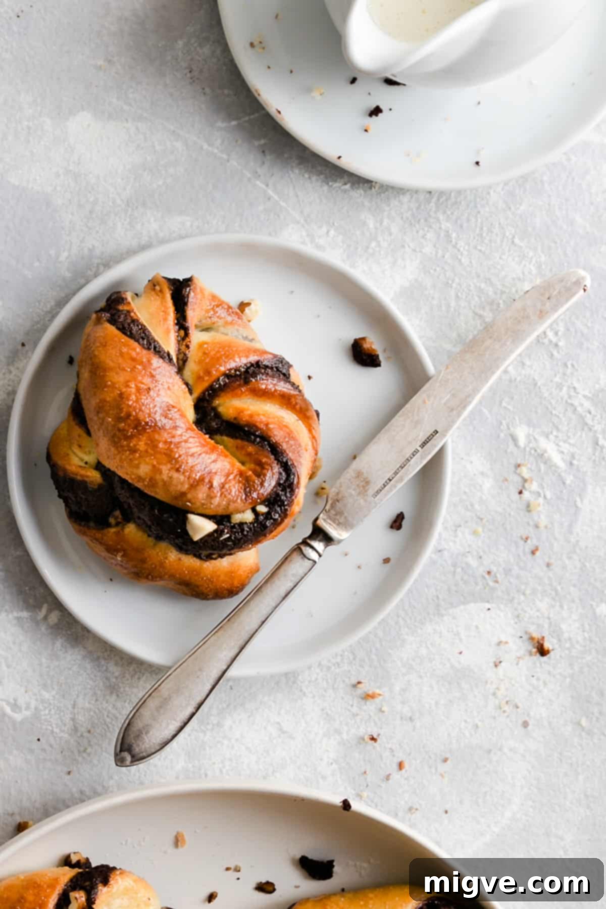 Swirled Chocolate Hazelnut Babka Buns 3 A close-up overhead shot of a single chocolate hazelnut babka bun on a small white plate, highlighting its intricate swirl and rich filling.