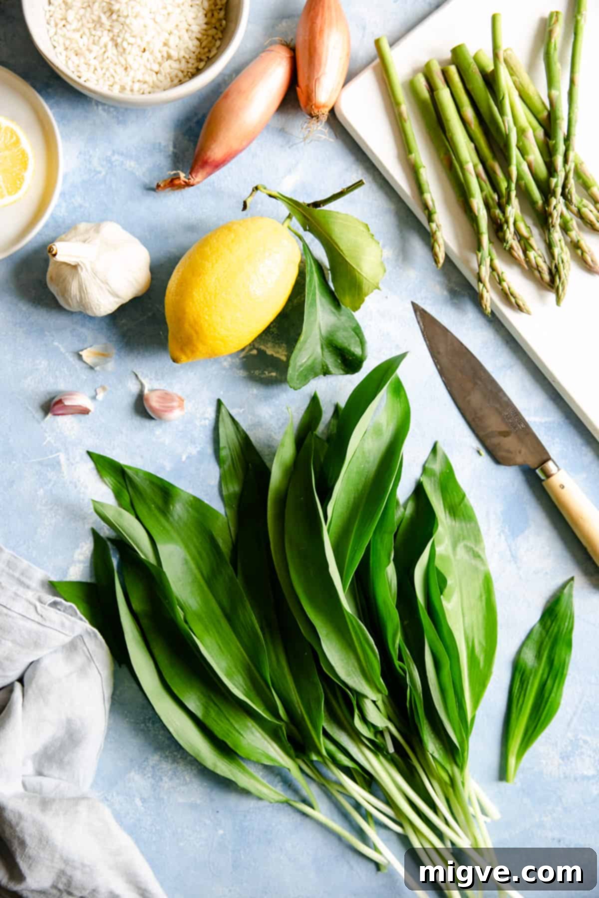 Overhead shot of the ingredients for wild garlic and asparagus risotto; fresh wild garlic, green asparagus, shallots, risotto rice