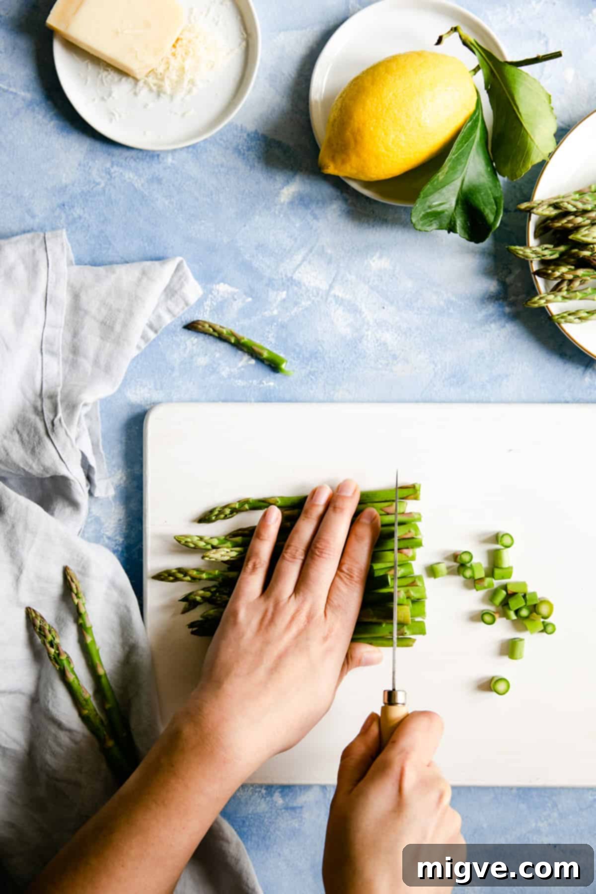 overhead shot of a person chopping the green asparagus on a white chopping board