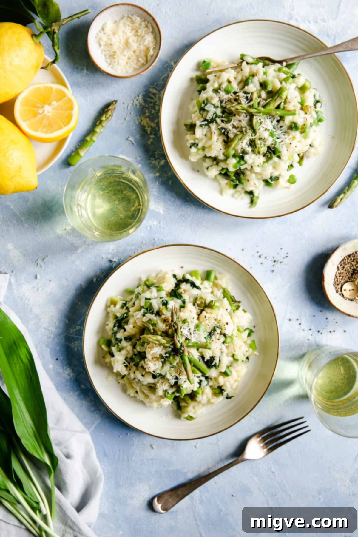 overhead shot of two bowls with wild garlic and asparagus risotto with a glass of white wine on side