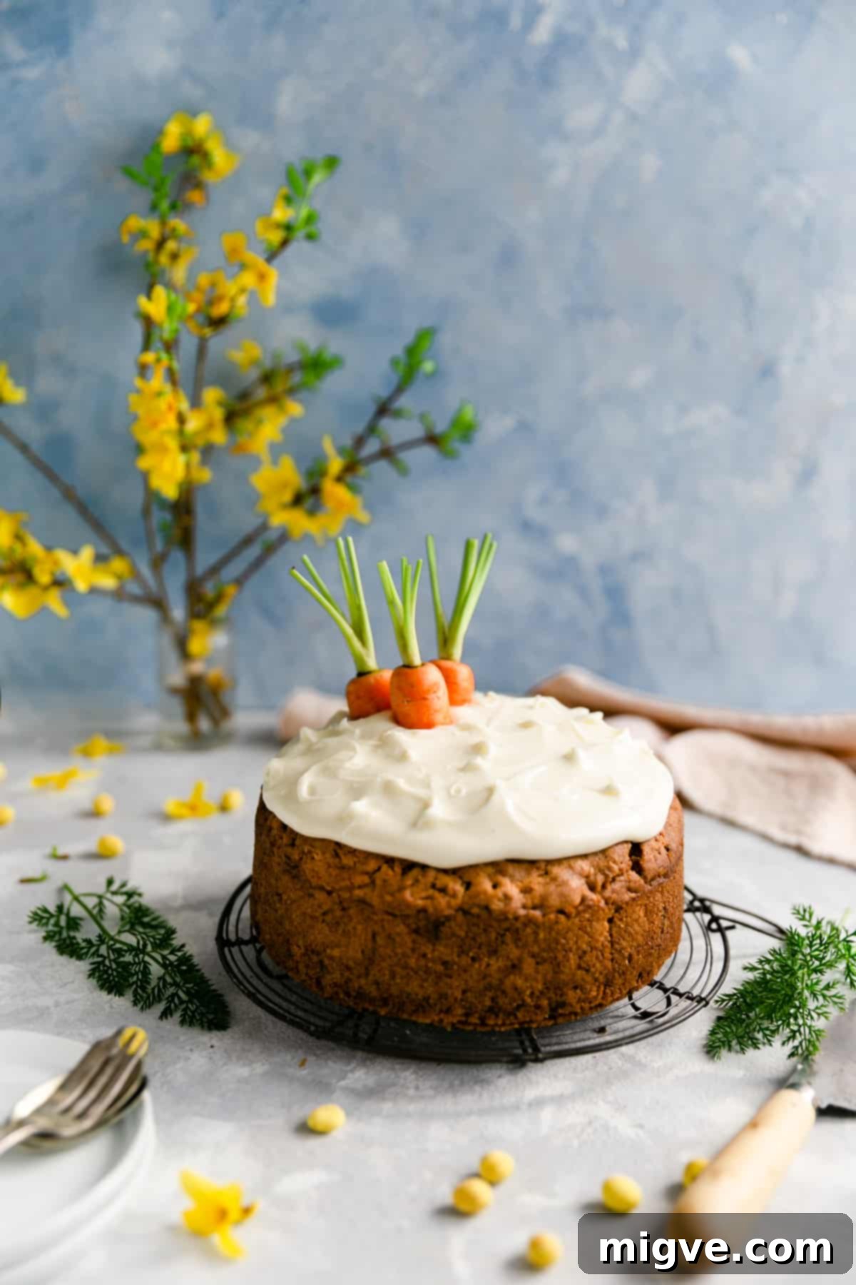 Delightful vegan carrot cake crowned with creamy, dairy-free cream cheese frosting and artfully adorned with fresh carrot tops.