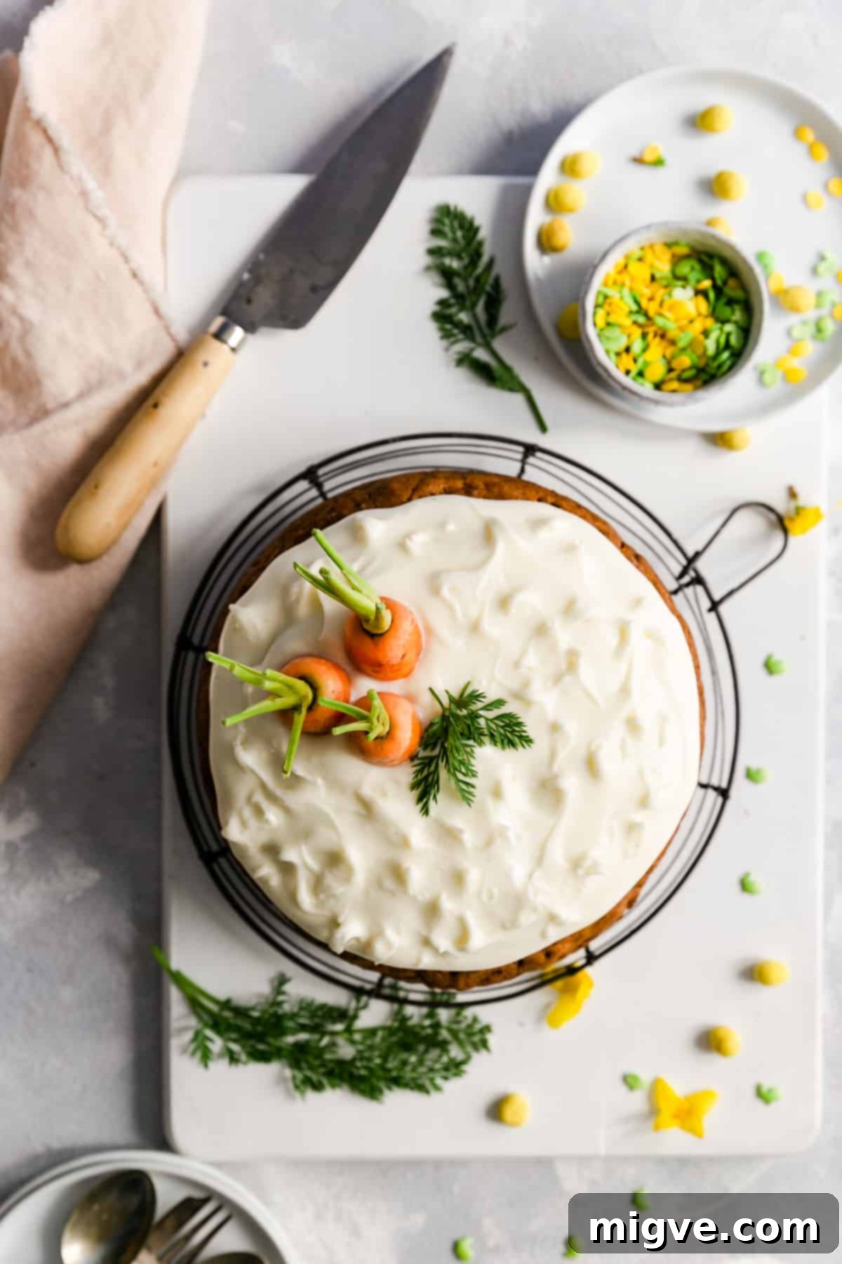 Overhead perspective of a beautifully frosted vegan carrot cake, featuring a generous layer of cream cheese frosting and delicate carrot tops as garnish.