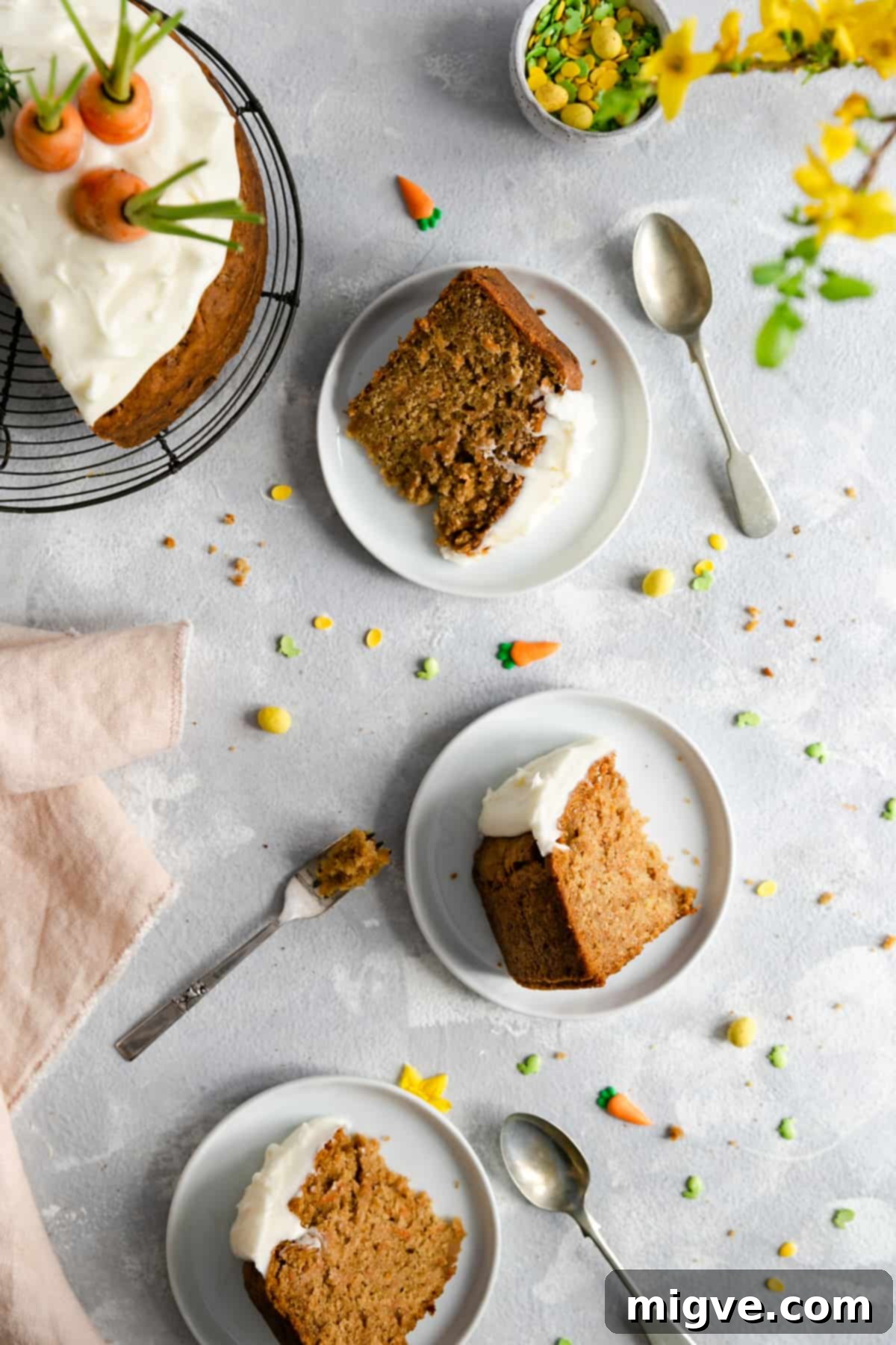Three individual slices of vegan carrot cake, each perfectly portioned and served on elegant small white plates with complementary cutlery.