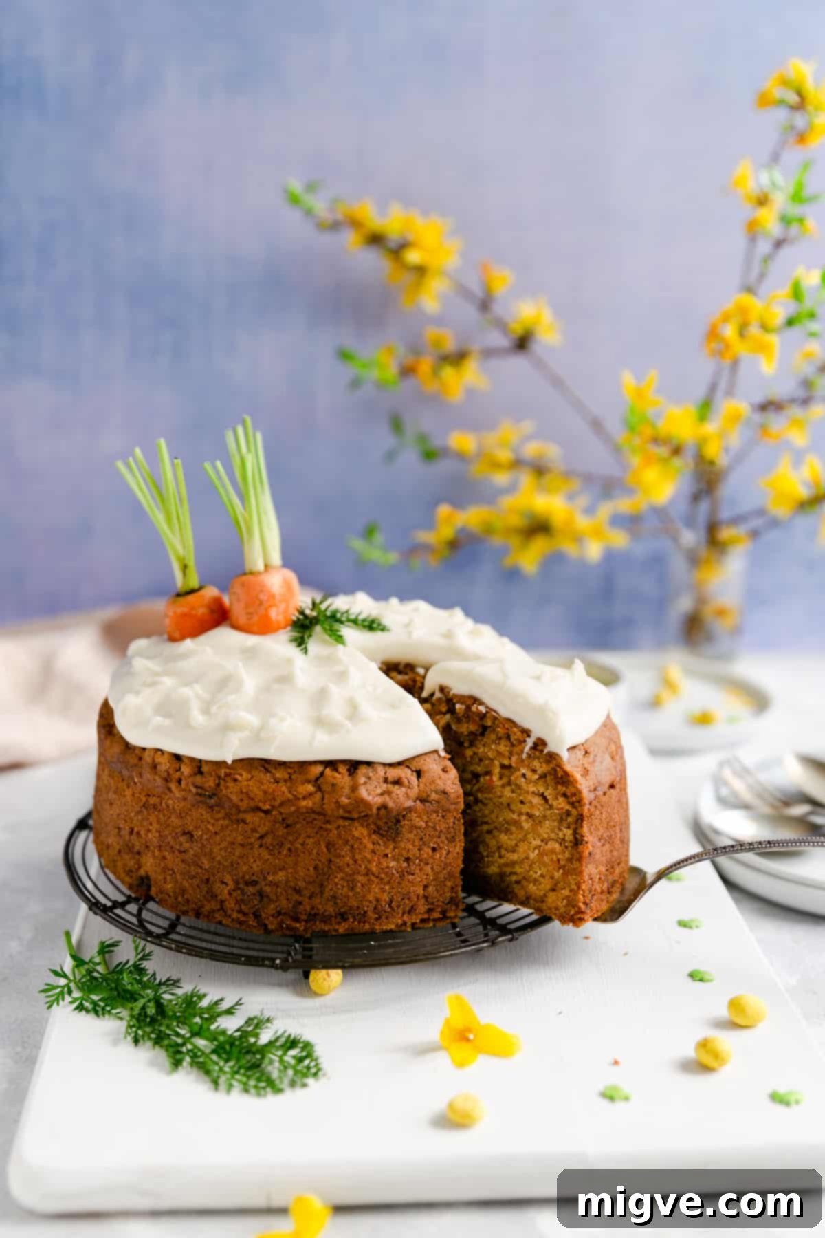 A tantalizing side view of the moist vegan carrot cake as a slice is carefully being cut out, revealing its inviting layers and texture.