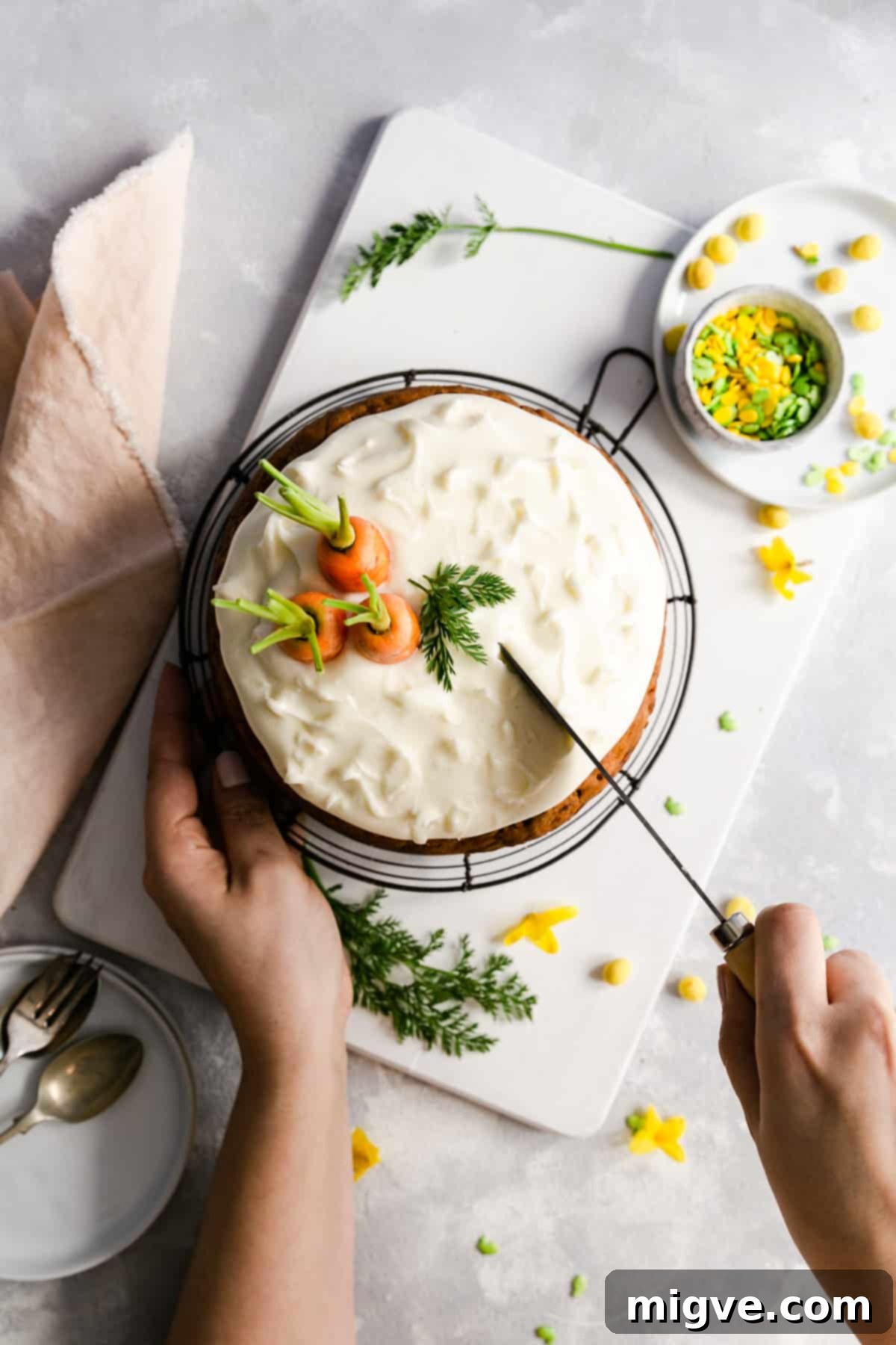 An inviting overhead shot of the fully frosted vegan carrot cake, with a hand delicately cutting into a slice, ready to be served.