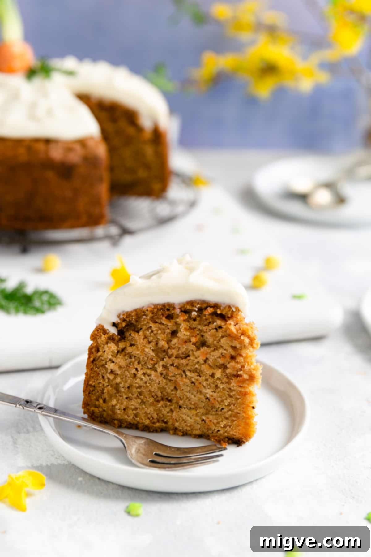 A perfectly portioned slice of vegan carrot cake, served on a small, elegant white plate, highlighting its moist interior and creamy frosting.