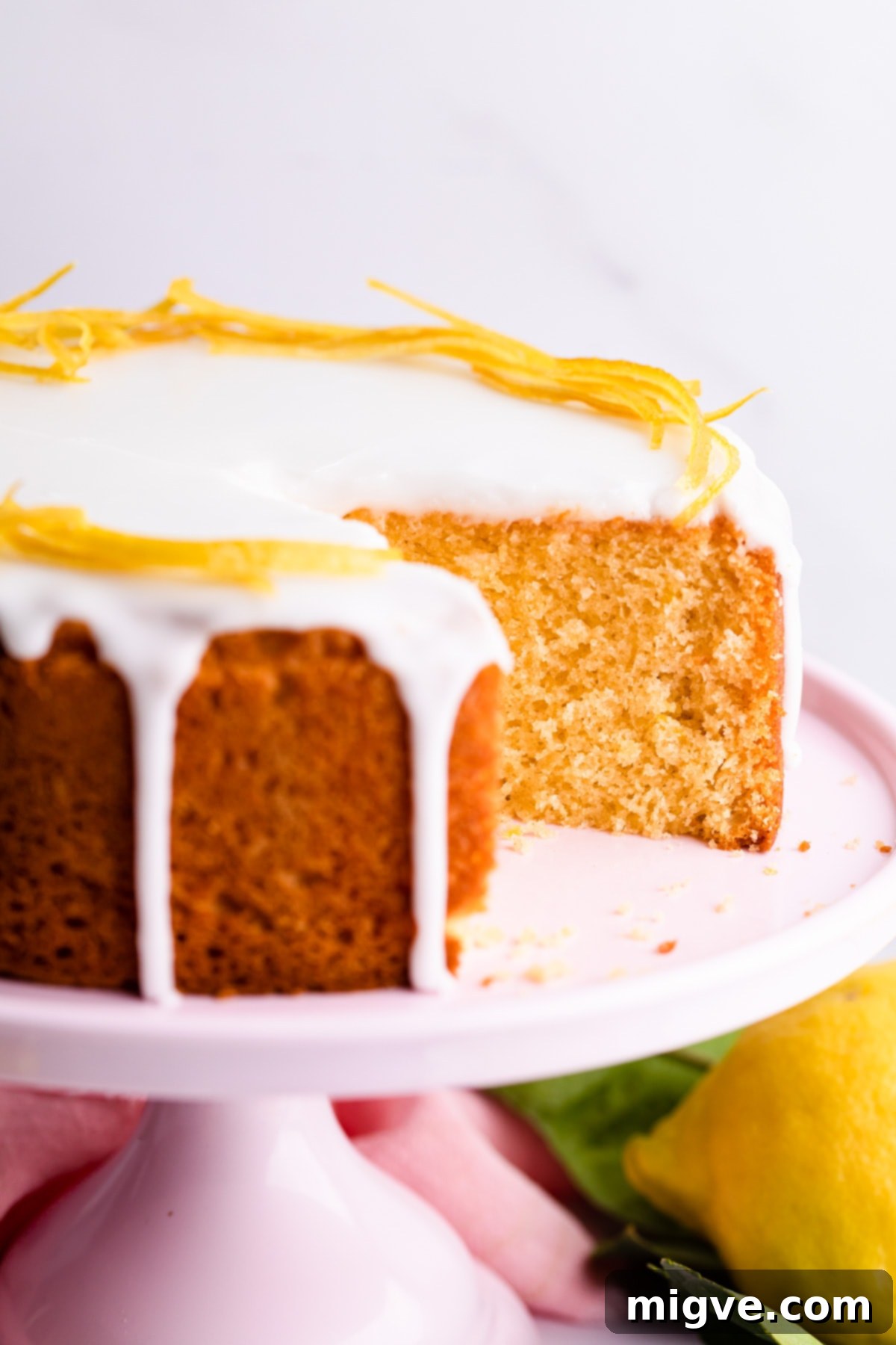 A slice cut out of a lemon sponge cake on a pink cake stand, revealing its fluffy and moist texture.
