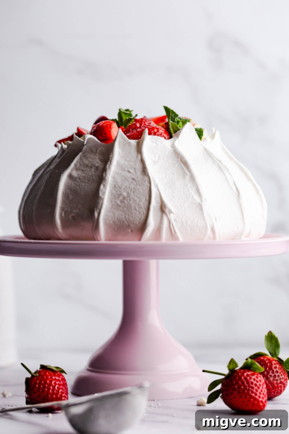 Straight-ahead view of a beautifully baked pavlova meringue shell sitting on a pink cake stand, showcasing its pristine white color and perfect shape