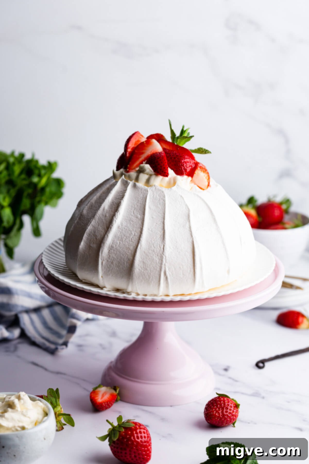 A 45-degree angle view of the vibrant strawberry pavlova elegantly displayed on a pink cake stand, highlighting its fresh toppings