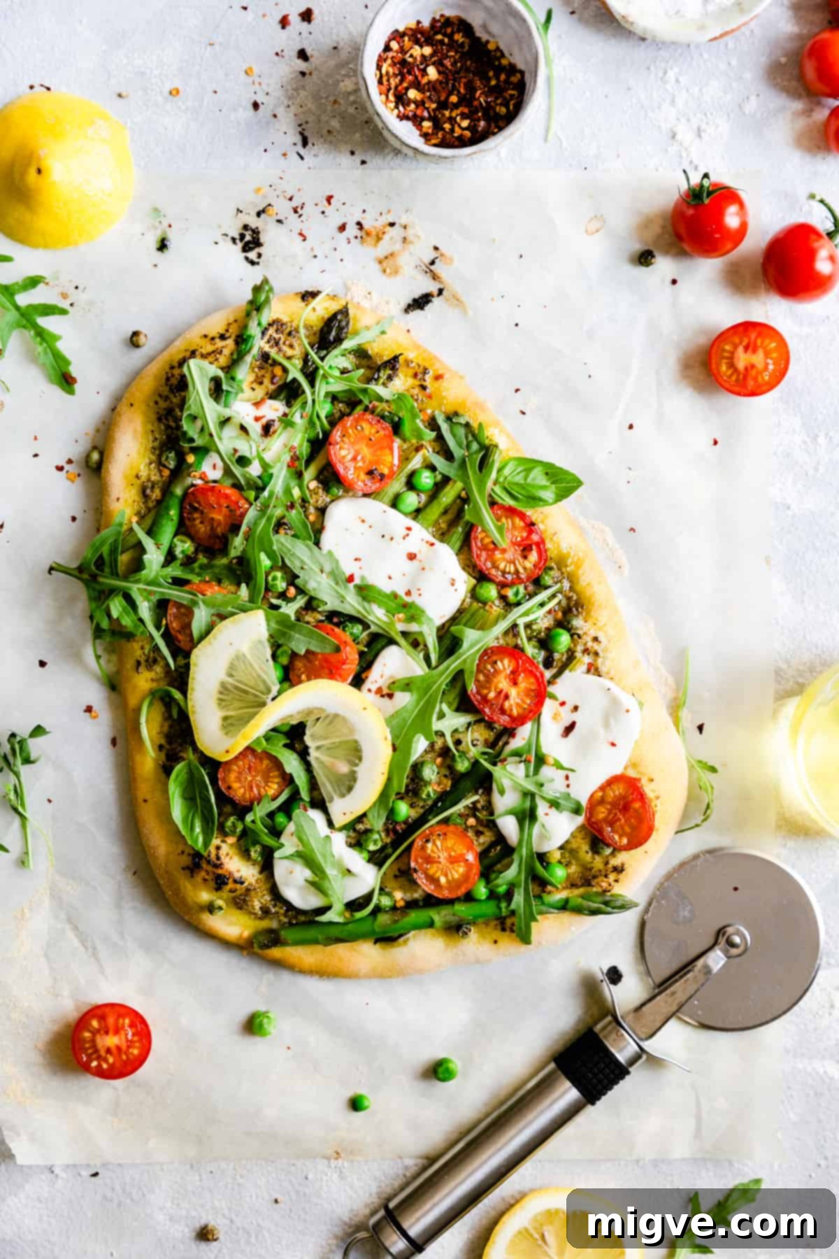 Overhead shot of a freshly baked homemade asparagus green pesto pizza, generously topped with vibrant green peas, halved cherry tomatoes, and a scattering of peppery rocket leaves, ready to be served.