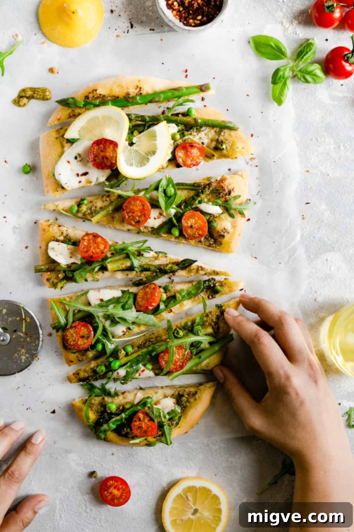 Top-down perspective of a hand reaching for a warm slice of freshly baked homemade asparagus green pesto pizza, capturing the irresistible moment of enjoyment.