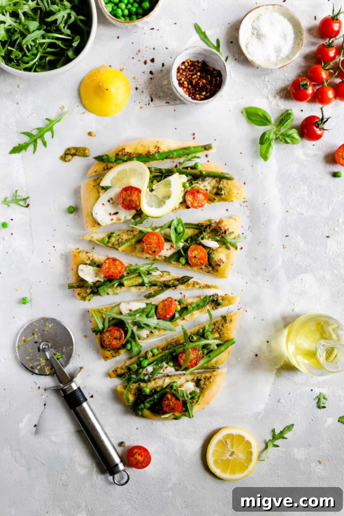Close-up overhead shot of a perfectly sliced asparagus green pesto pizza, revealing its golden-brown crust and fresh toppings including vibrant green asparagus spears, juicy cherry tomatoes, and fresh rocket.