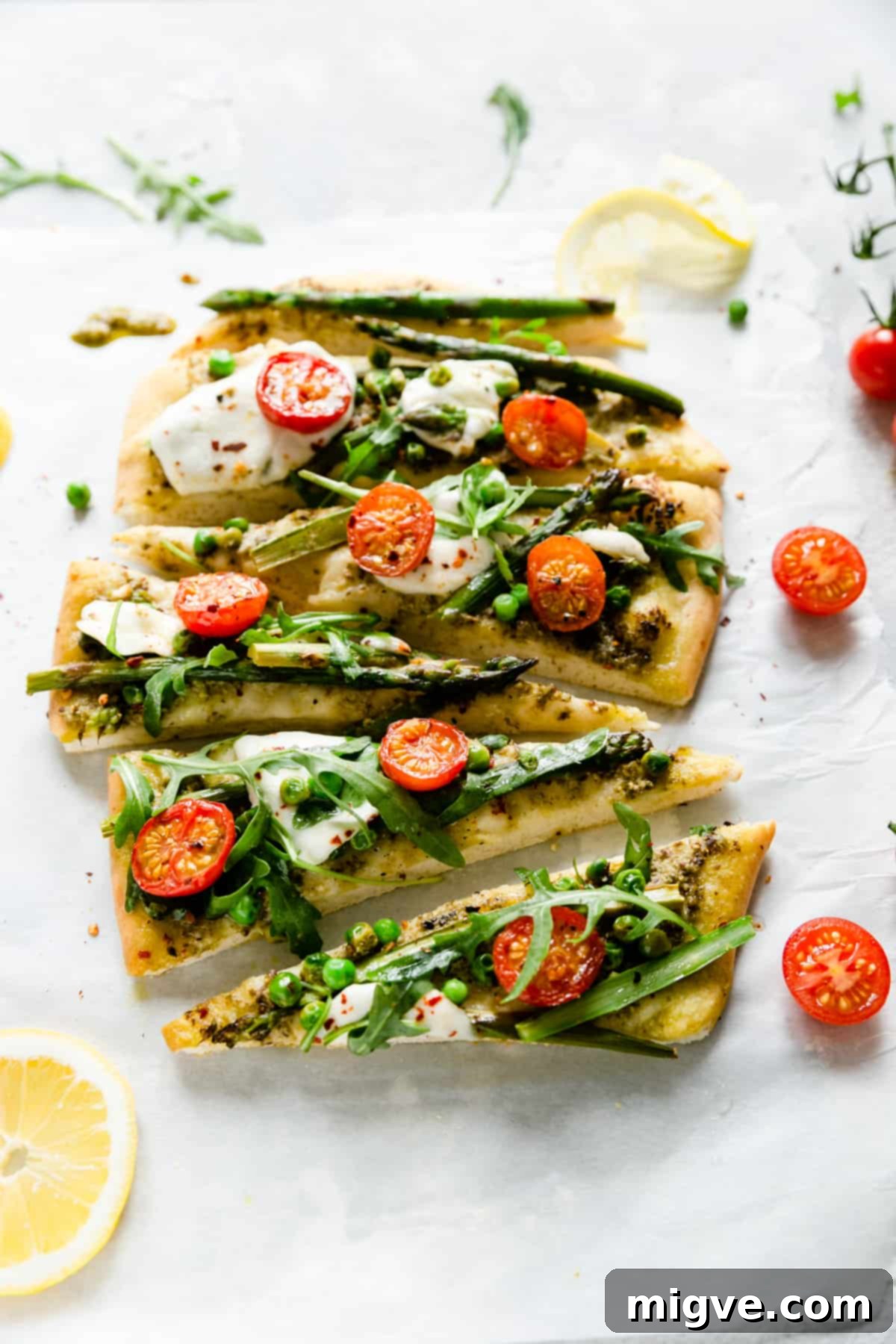 Close-up shot of individual triangle slices of asparagus green pesto pizza, beautifully topped with cherry tomatoes, melted mozzarella, and fresh rocket, highlighting the delicious textures.