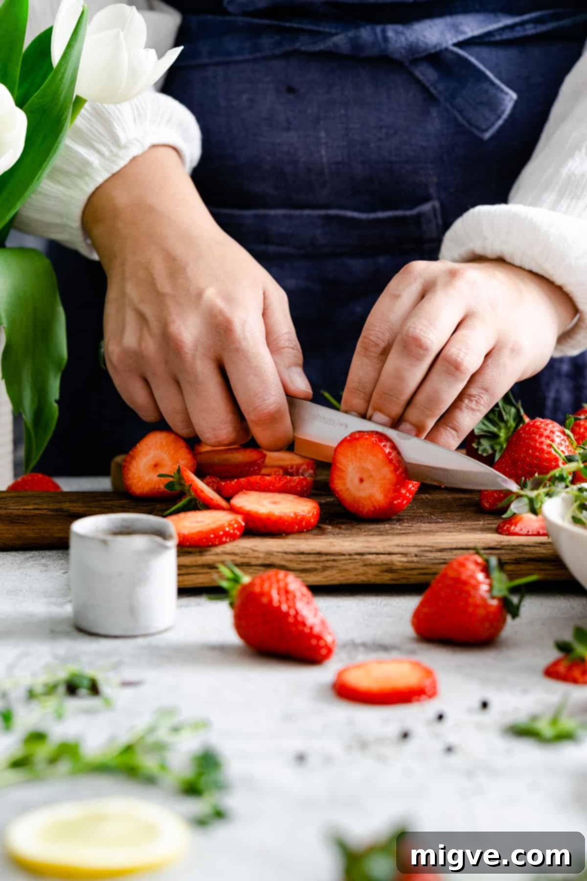 Rustic Strawberry Galette 9 a close up of a person's hands slicing strawberries on a wooden chopping board