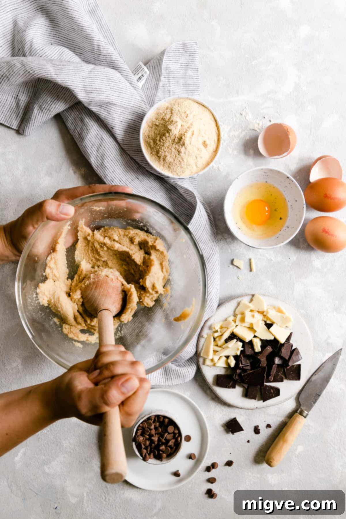 Overhead shot of a person vigorously beating softened butter and two types of sugar in a large bowl, creating a light and fluffy mixture.