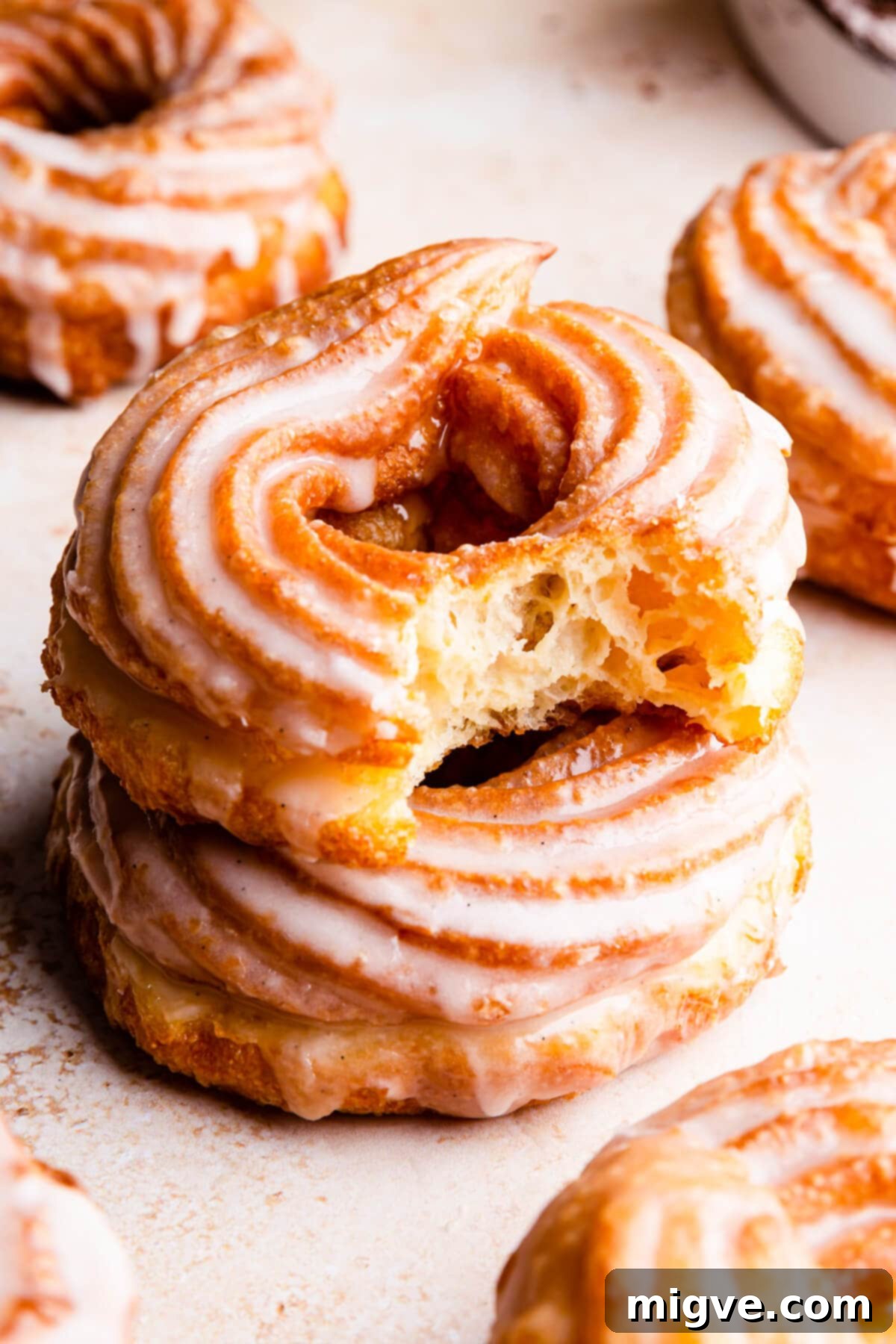 Airy Choux Rings 2 Close-up side view of a glazed French cruller doughnut with a bite taken out, resting on top of another doughnut, highlighting its delicate texture and golden-brown color.