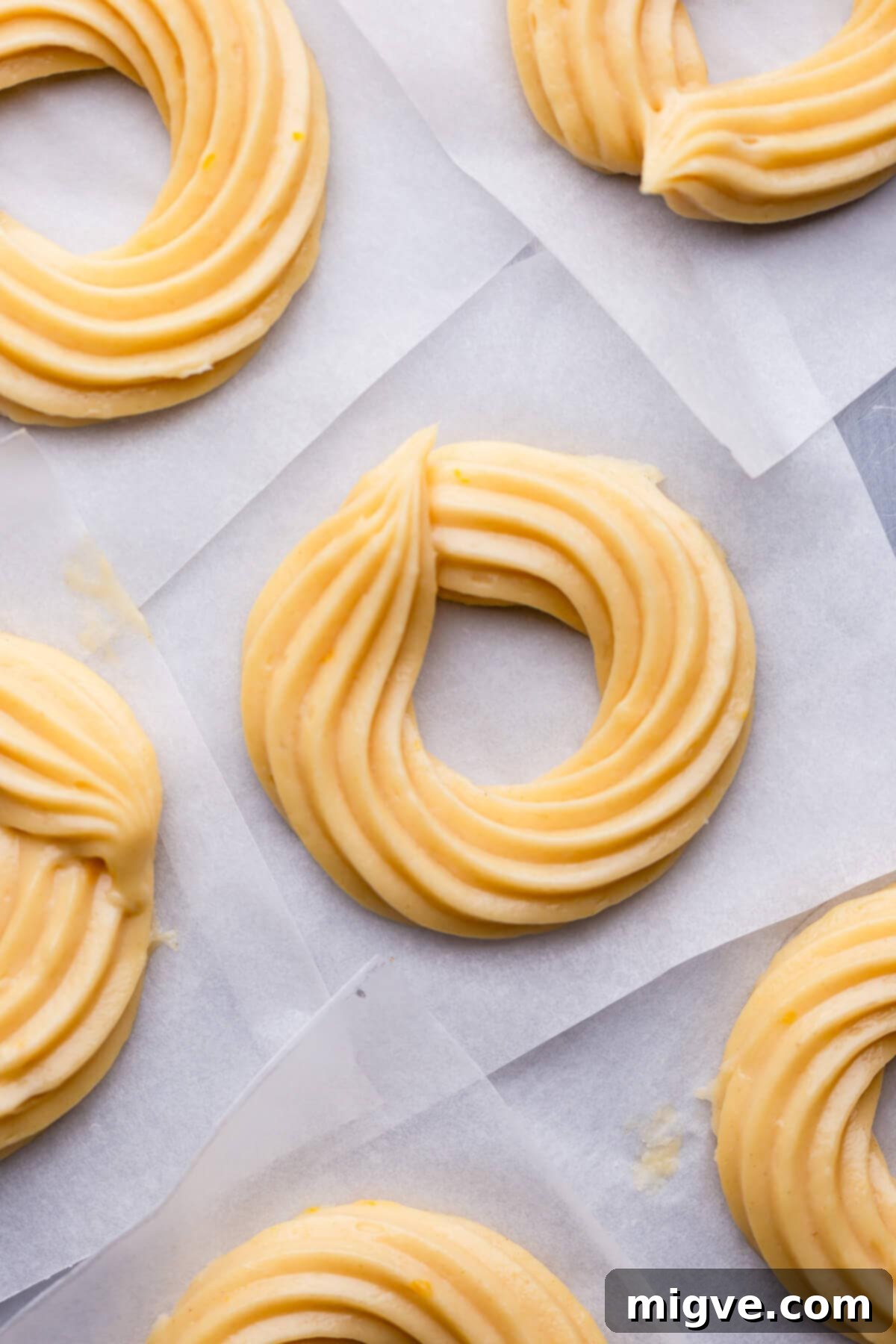 Airy Choux Rings 5 Overhead view of raw French cruller doughnuts neatly piped onto individual squares of parchment paper, ready for frying.