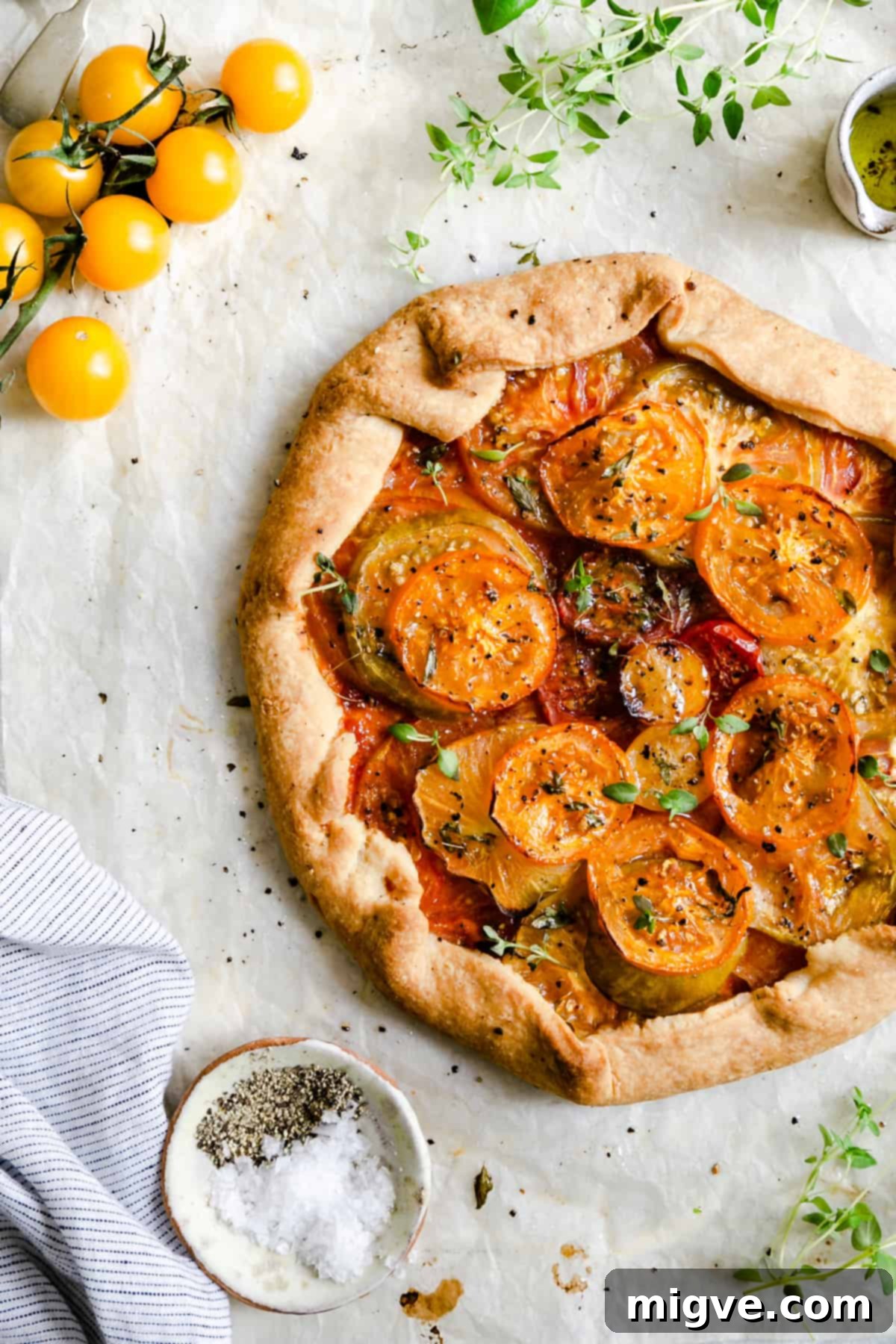 overhead shot of a golden-brown summer tomato galette adorned with fresh thyme and a sprinkle of black pepper
