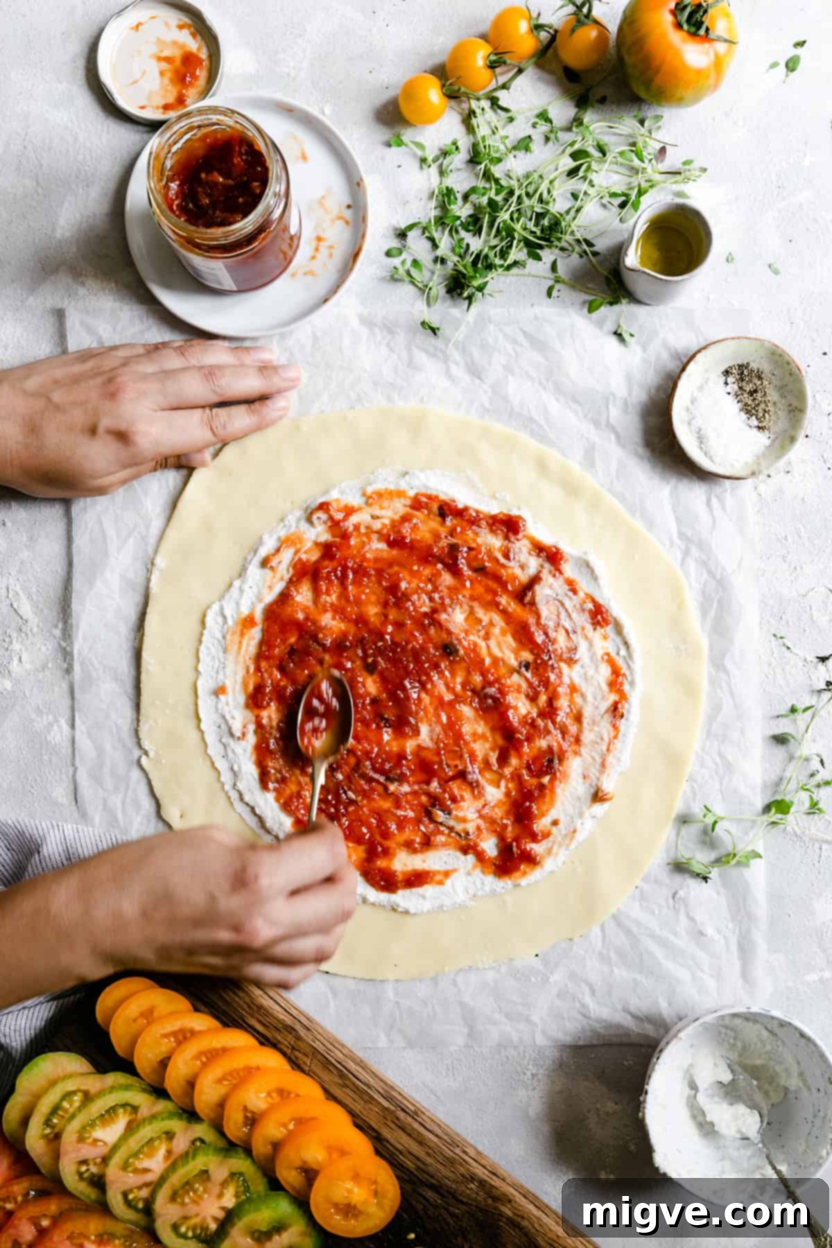overhead shot of hands carefully spreading vibrant tomato jam onto a creamy ricotta base on a galette crust