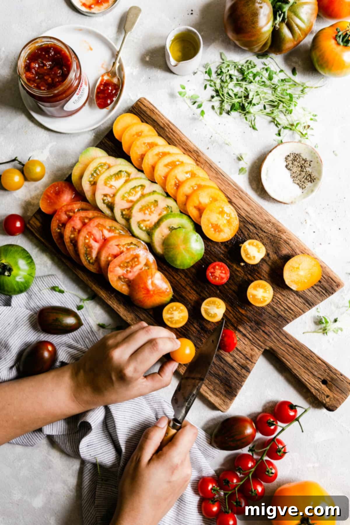top view of a person meticulously slicing a variety of fresh, ripe tomatoes on a sturdy wooden chopping board