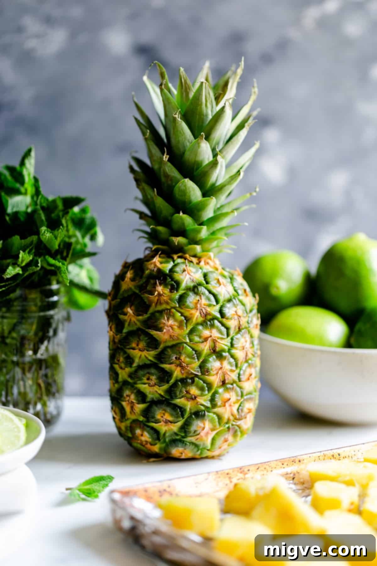A large, ripe fresh pineapple sits beside a small bunch of vibrant fresh mint, ingredients for a delicious tropical cocktail.