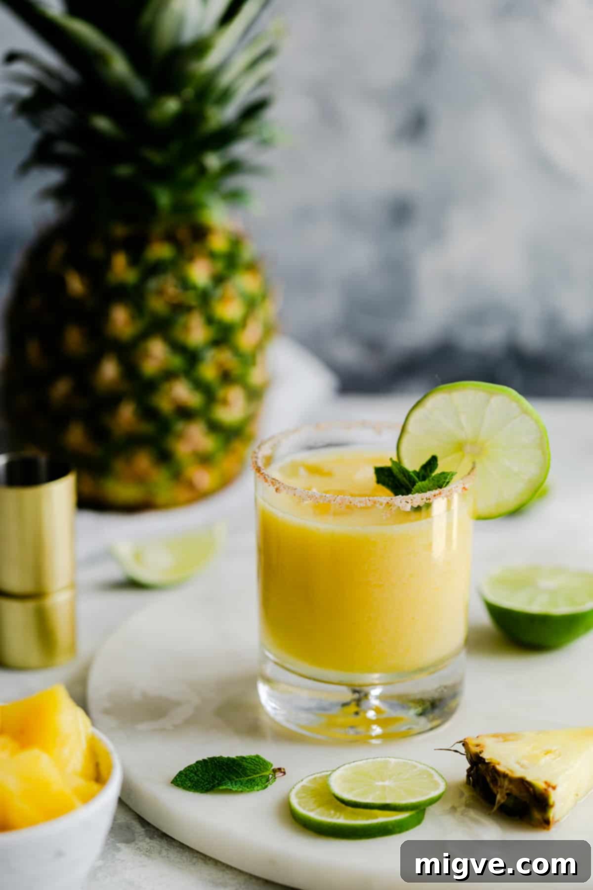 A single glass of frozen pineapple margarita, garnished with a vibrant lime slice, standing elegantly on a marble surface.