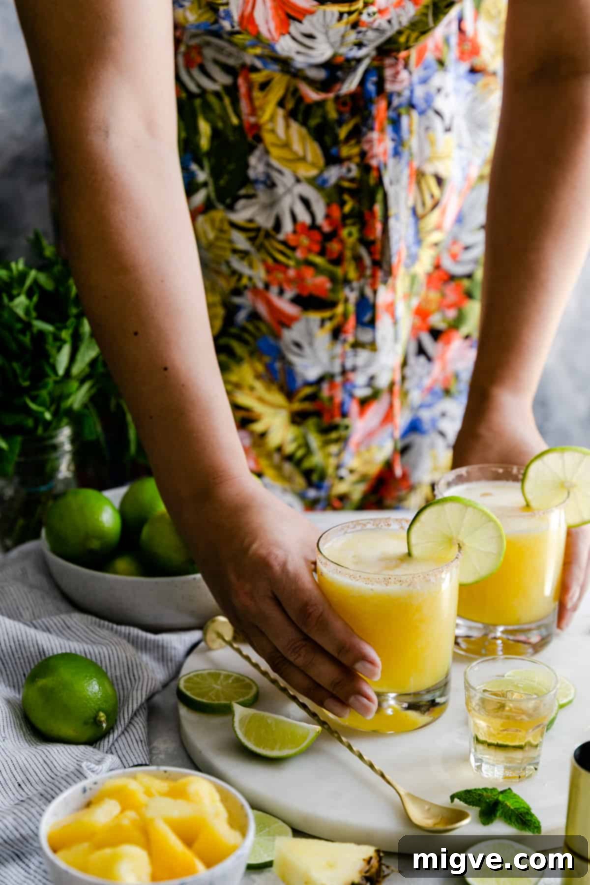 A person holding two vibrant glasses of frozen pineapple margaritas, inviting a toast to summer.