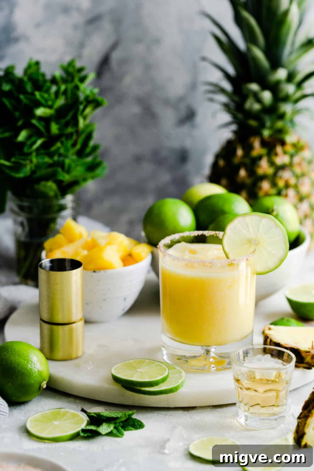 A single glass of frozen pineapple margarita, perfectly garnished, sitting on a marble chopping board.