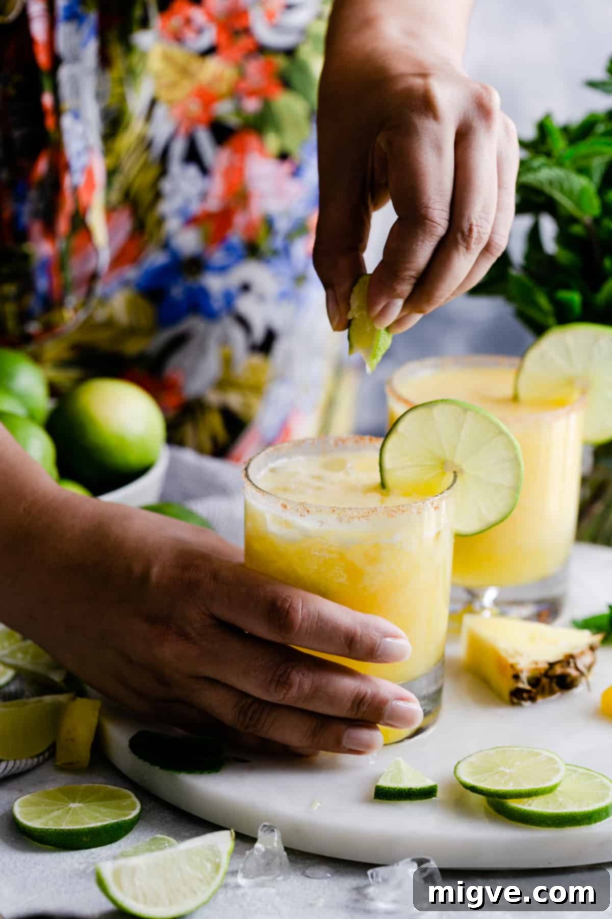 A hand gracefully squeezing a fresh lime slice into a glass of frozen pineapple margarita, adding the final touch of zest.