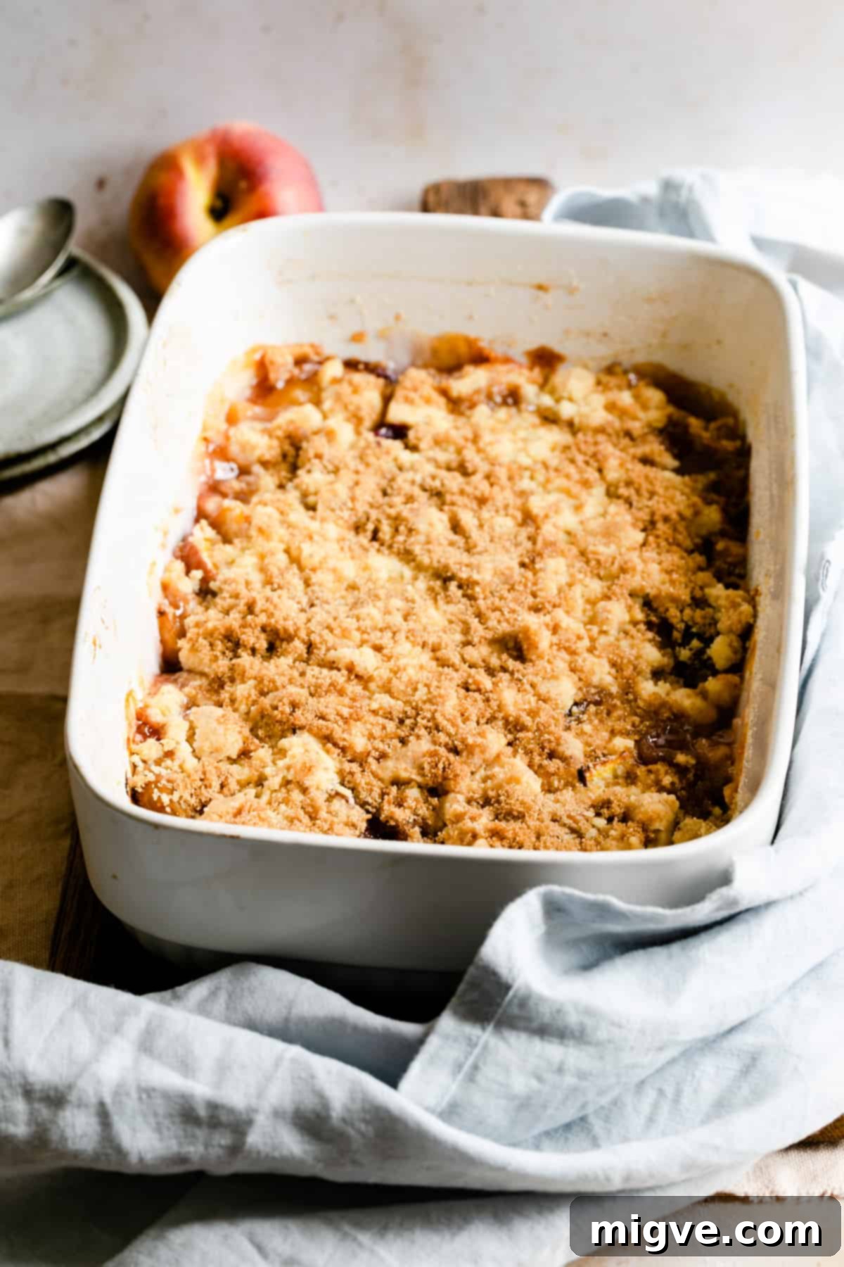 a freshly baked peach cobbler in a white ceramic dish, golden brown and bubbly