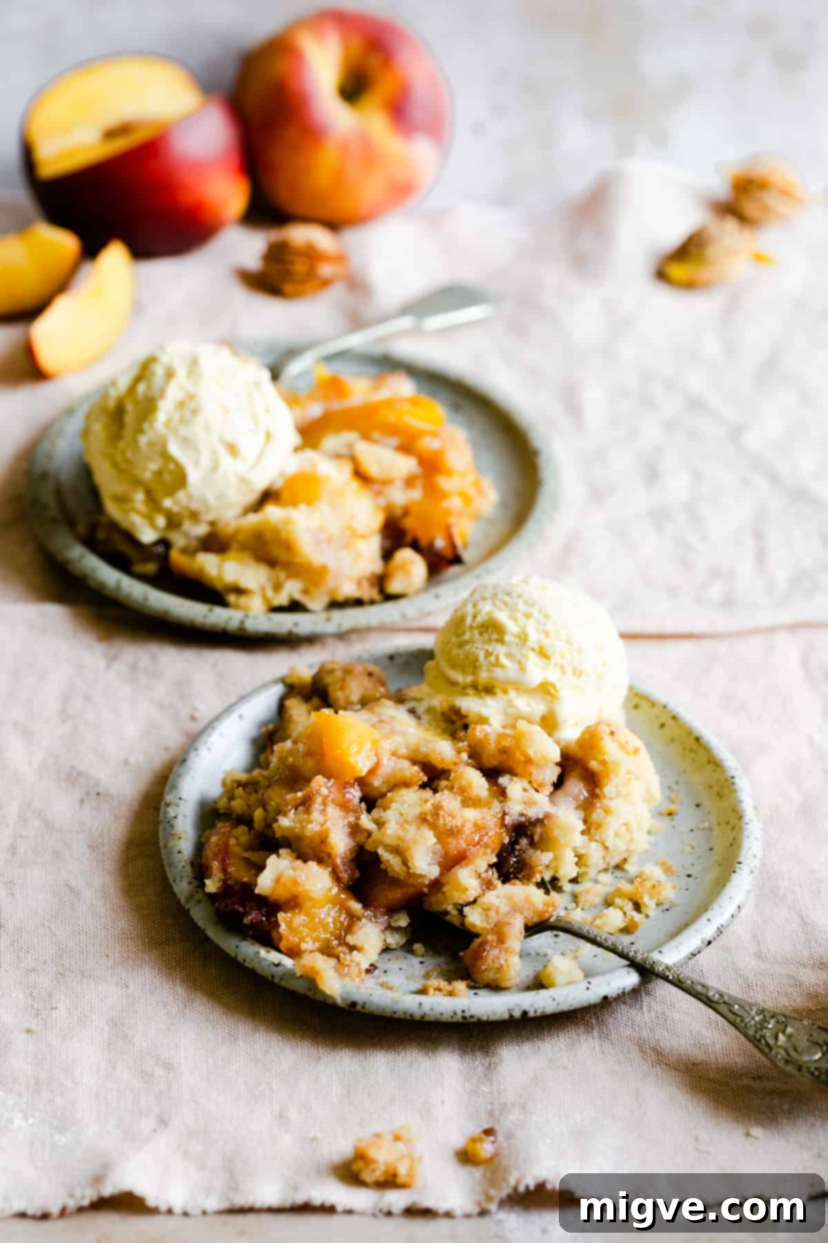 two generous portions of peach cobbler served in bowls with a scoop of vanilla ice cream