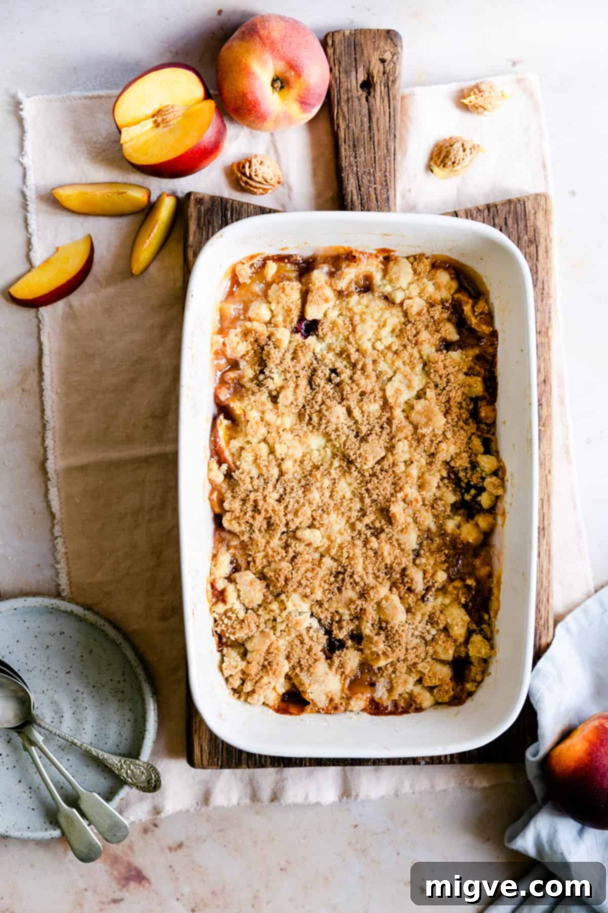 overhead shot of a golden-brown peach cobbler cooling on a wooden chopping board