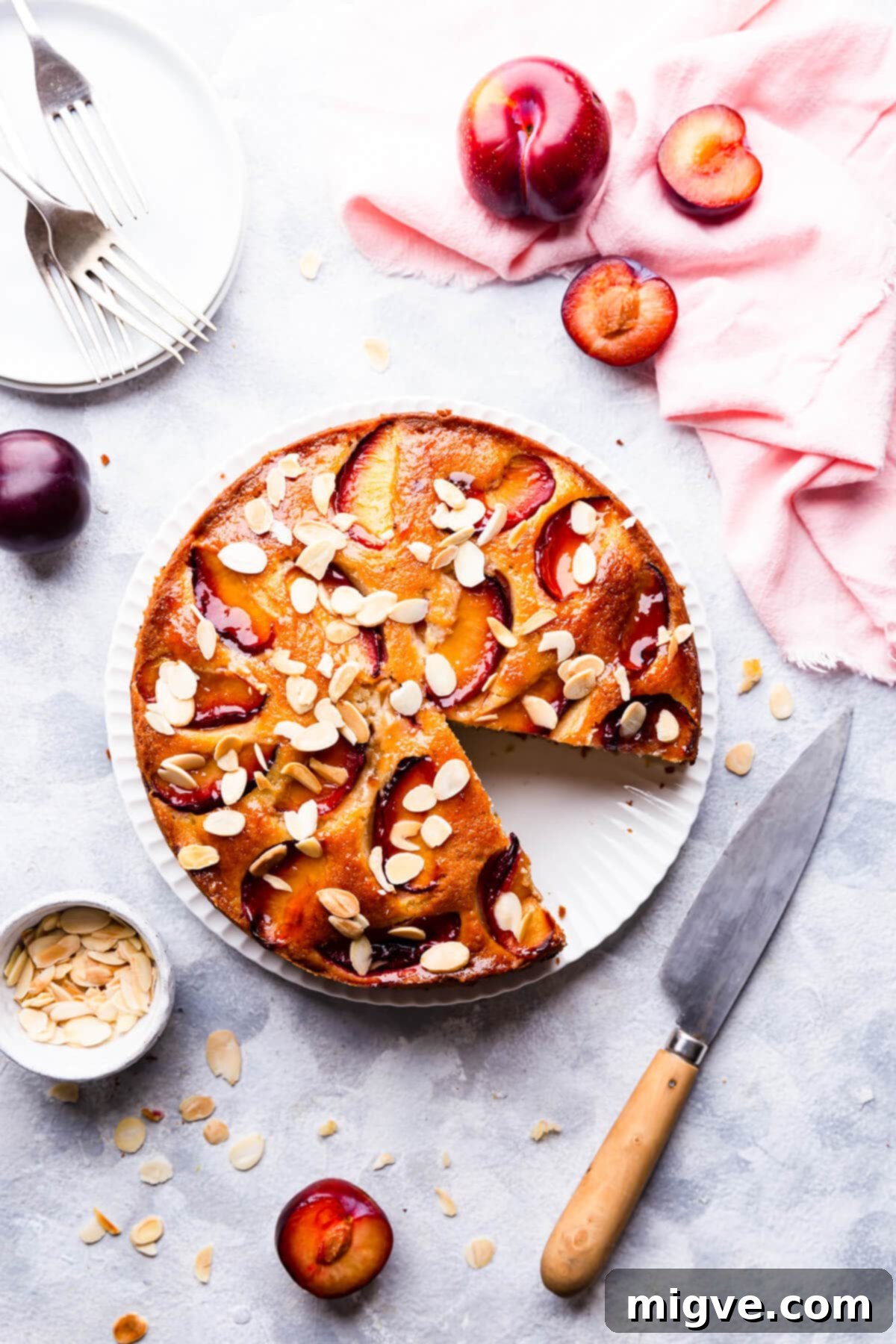 top view of plum and almond cake with a slice cut out, showcasing its moist texture and juicy plums