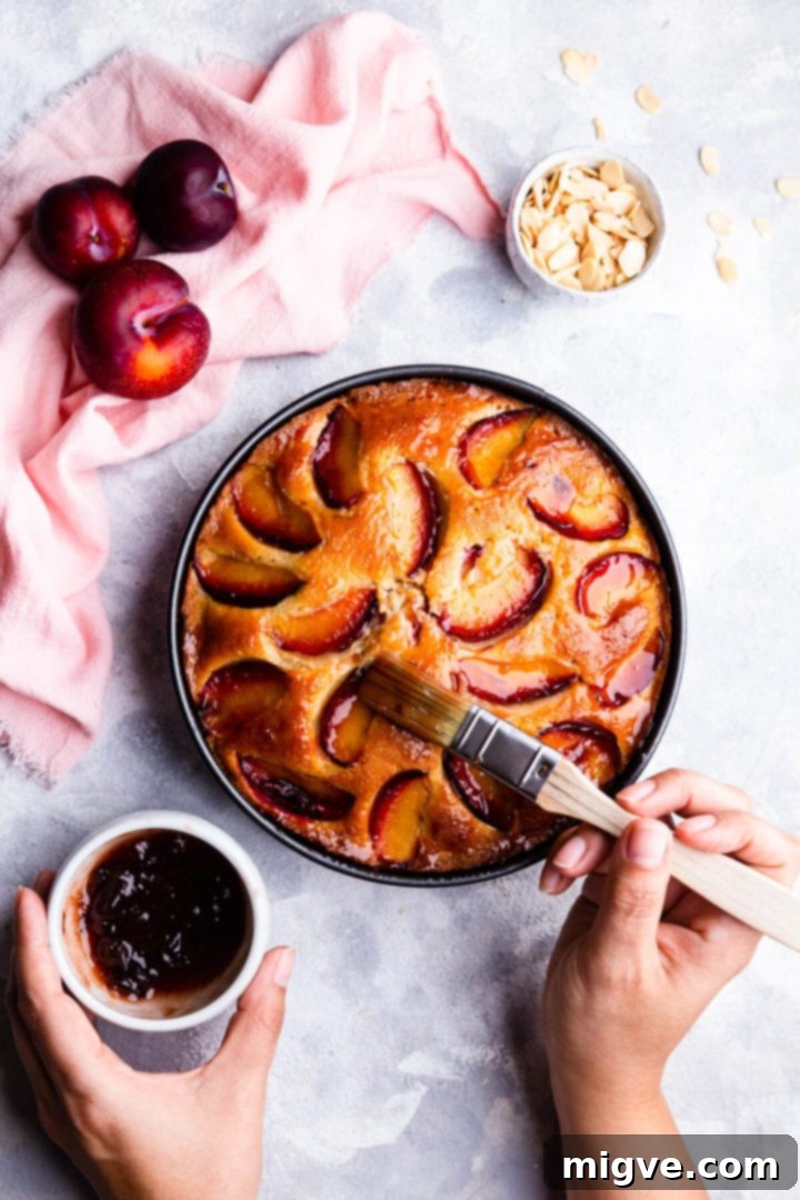 top view of a person brushing baked plum and almond cake with some jam