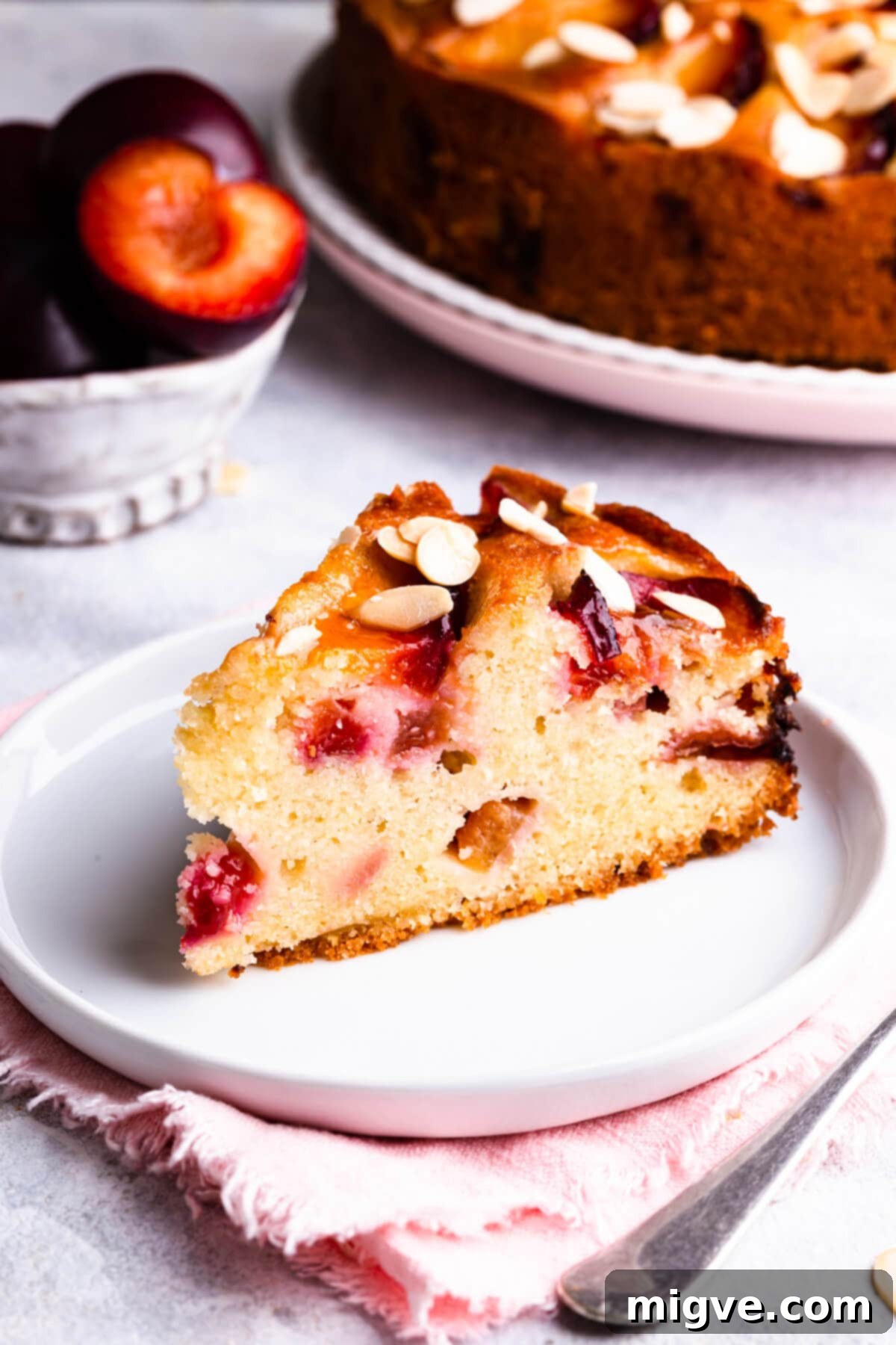 side super close up at one slice of plum and almond cake on a white plate, showing the layers and fruit