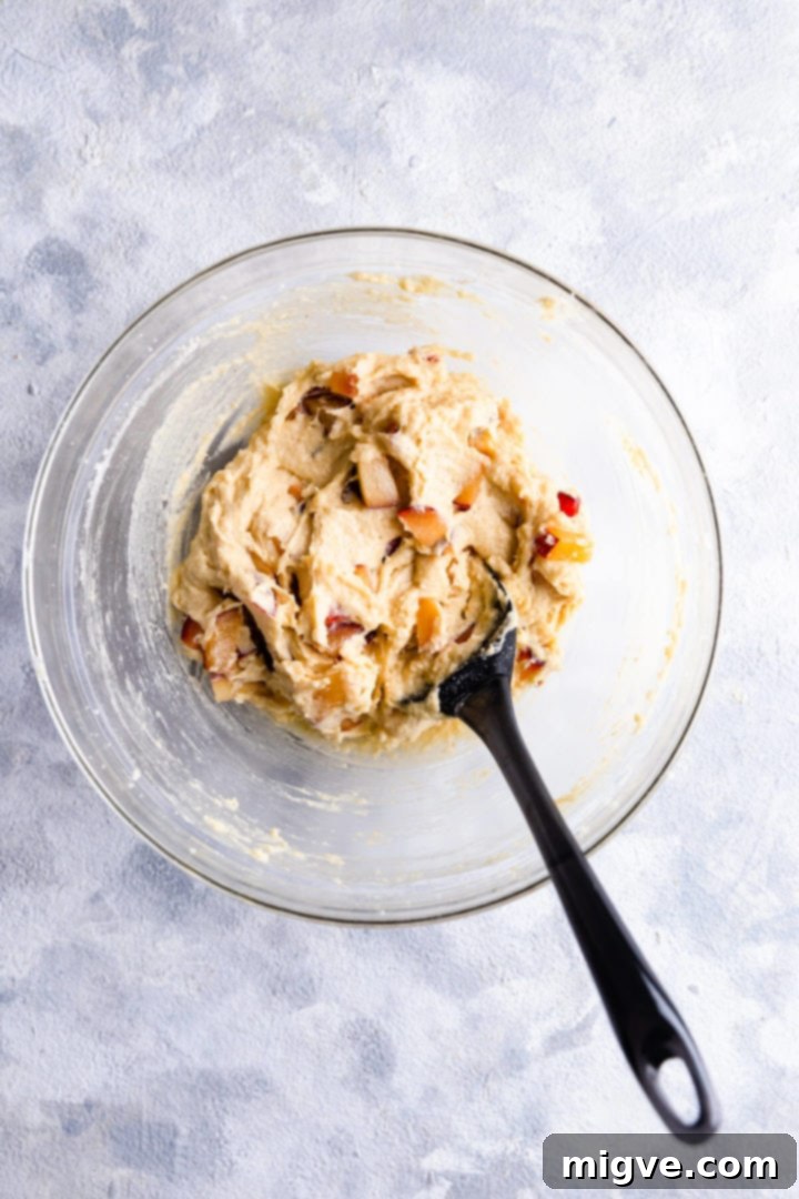 overhead shot of cake batter in a bowl mixed with chopped plums