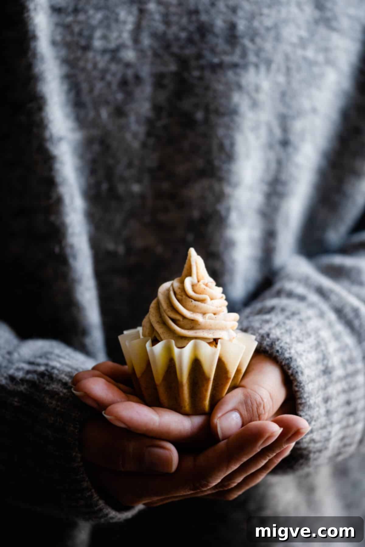 straight ahead shot of a person holding a cupcake in their hands, highlighting the fluffy frosting