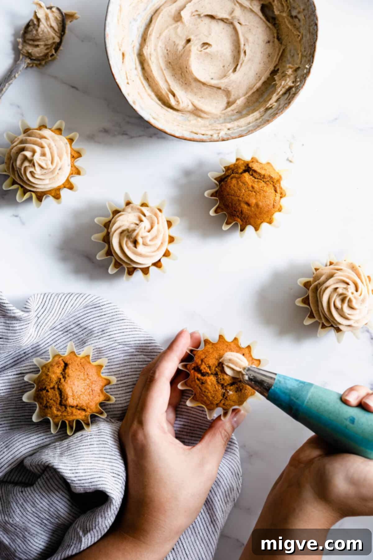 a person piping chai frosting on top of pumpkin cupcakes, demonstrating the finishing touch