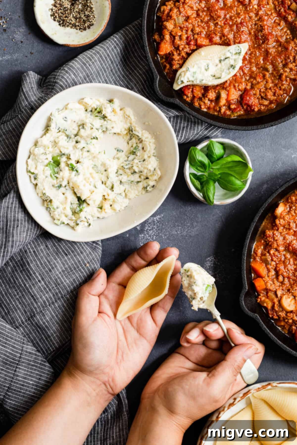 overhead shot of a person stuffing pasta shells with creamy cheese mixture