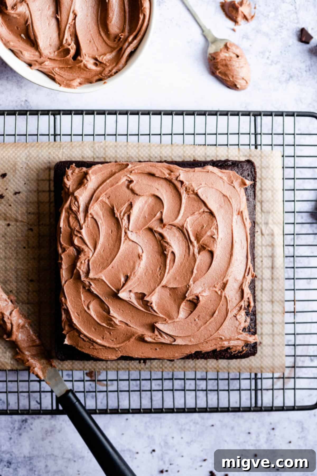 Overhead view of a beautiful square dark chocolate cake, perfectly frosted and resting on a wire rack to set.