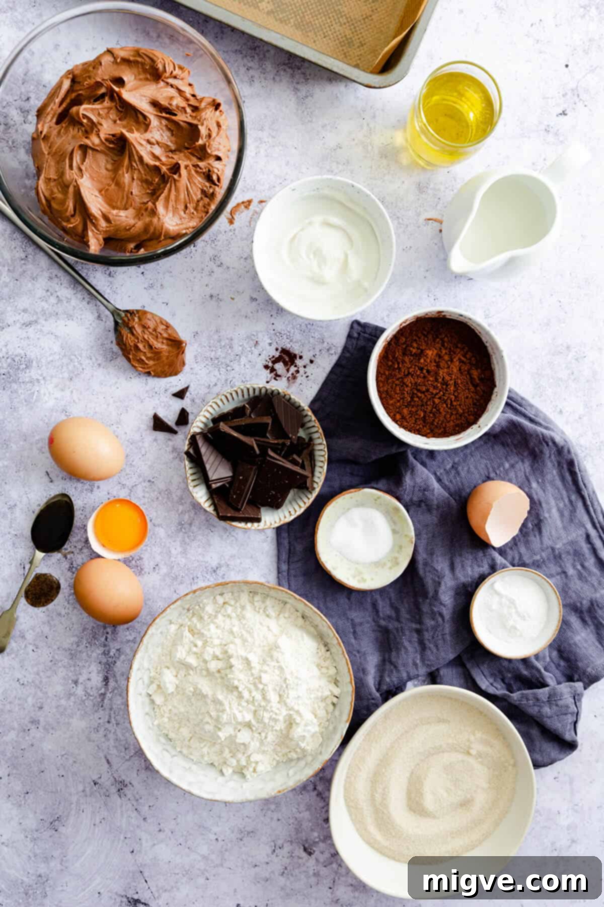 Overhead shot displaying an array of high-quality ingredients laid out for making a dark chocolate traybake, including chocolate, flour, eggs, and coffee.