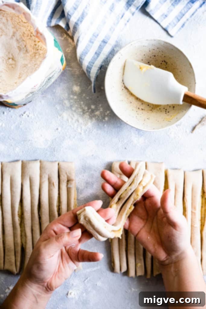 Top-down view of a person holding a single strip of dough, ready to begin shaping.