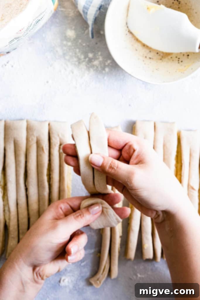 Overhead shot of hands in the process of shaping a cardamom bun, twisting the dough.